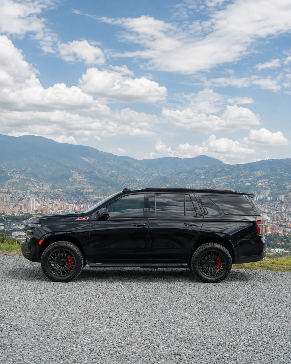 Full side profile of the black Chevrolet Tahoe on gravel, with the mountains behind.