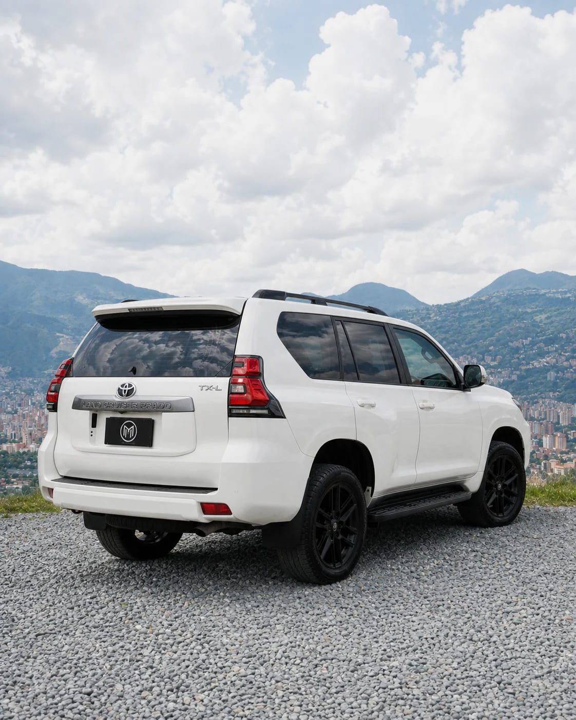 White Toyota Prado in rear three-quarter view, tailgate and lights in shot, with Medellín behind.